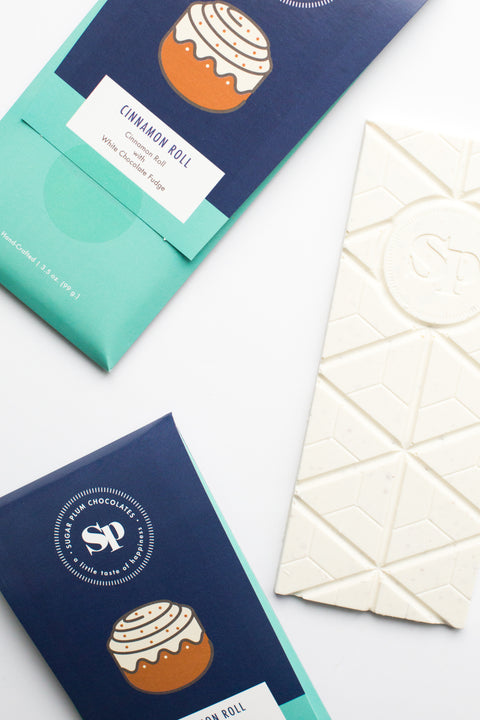 Cinnamon Roll White Chocolate Bars packaging and white chocolate square, showcasing graham cracker and sticky bun flavors.