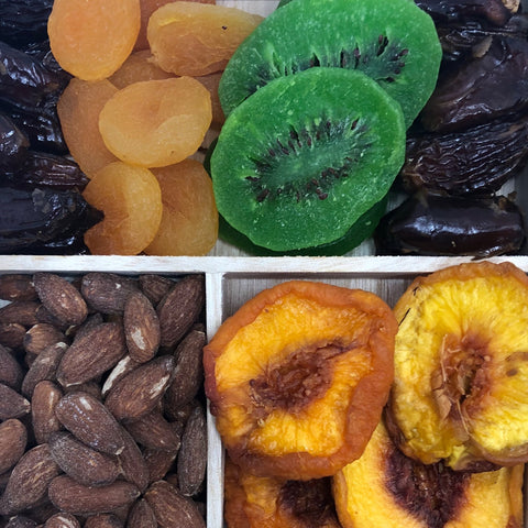 Gourmet dried fruit and nut tray with apricots, kiwis, dates, almonds, and peaches on a wooden platter.