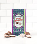 Festive box of milk chocolate holiday nonpareils with scattered peppermint snowflake chocolates on a white tiled background.